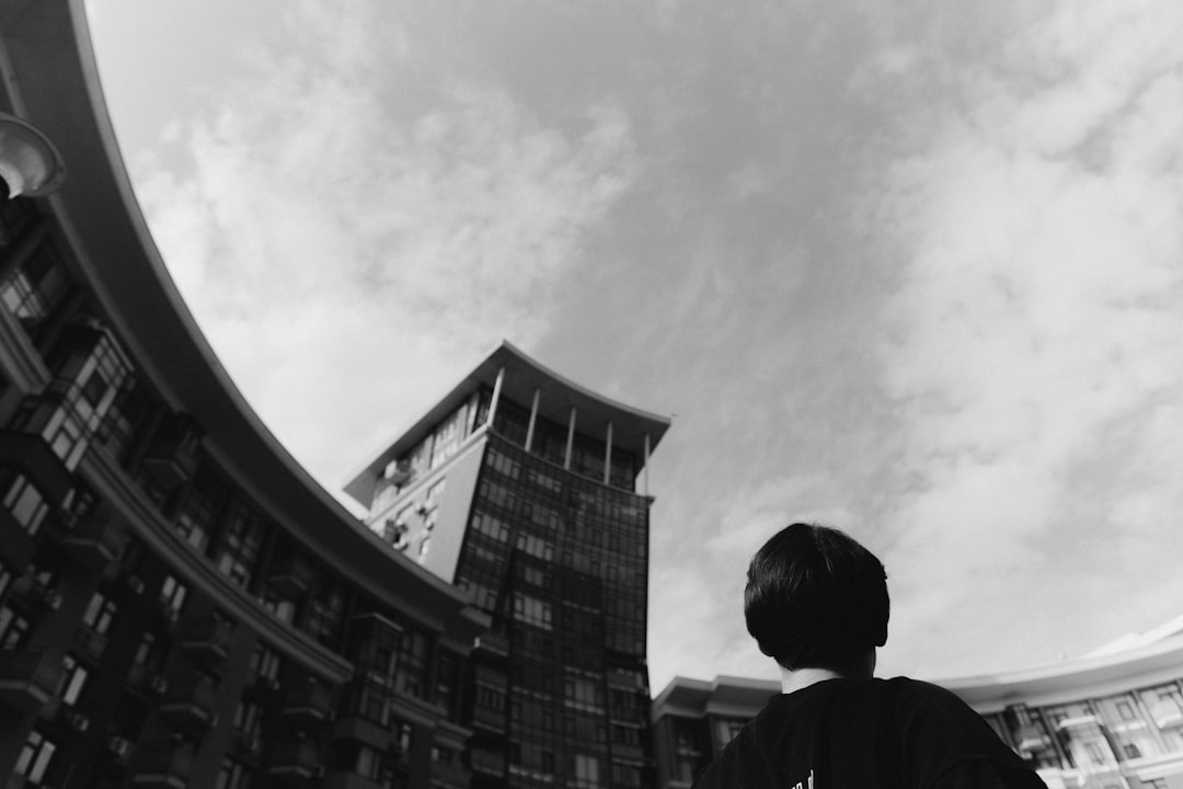 grayscale photo of man in black jacket standing near building