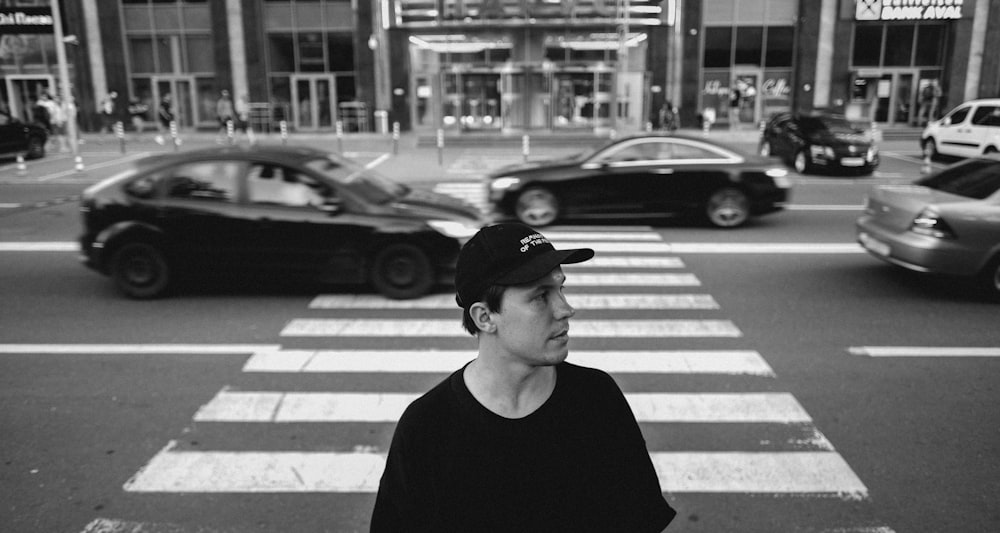 man in black crew neck shirt wearing black cap standing on pedestrian lane during daytime