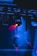 Multiple stage lights suspended from a metal framework illuminate the scene with beams of red light, contrasting against a predominantly blue-lit background. The image creates a dramatic, high-energy ambiance typical of concert or theatrical settings.