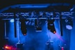 A stage setup featuring various lighting equipment with trusses overhead. The lights emit blue and red colors, creating a dynamic and vibrant ambiance. Smoke or haze adds a dramatic effect to the scene.