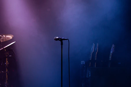 A warmly lit stage with amber spotlights casting a cozy glow over a sleek microphone, framed by textured brick walls and subtle neon pink accents.