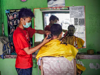 man in red crew neck t-shirt cutting the hair of the man