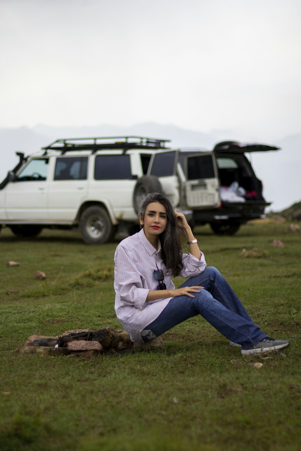 woman in white long sleeve shirt and blue denim jeans sitting on green grass field during