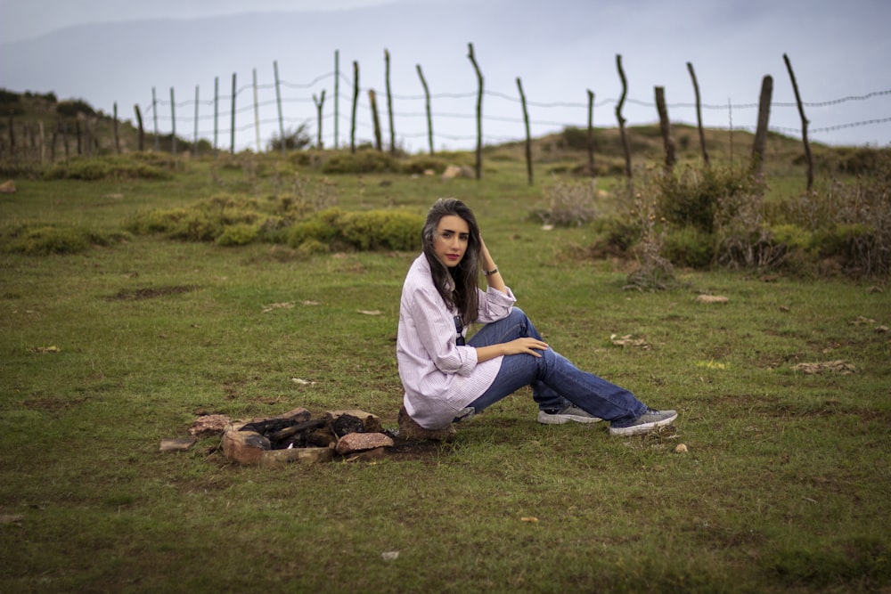 woman in white long sleeve shirt and blue denim jeans sitting on green grass field during