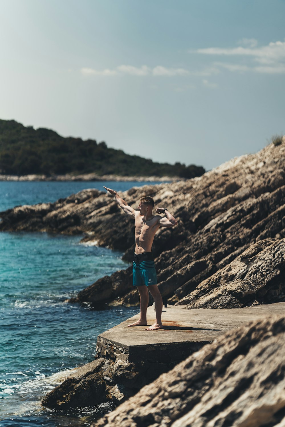 man in blue shorts standing on brown rock formation near body of water during daytime