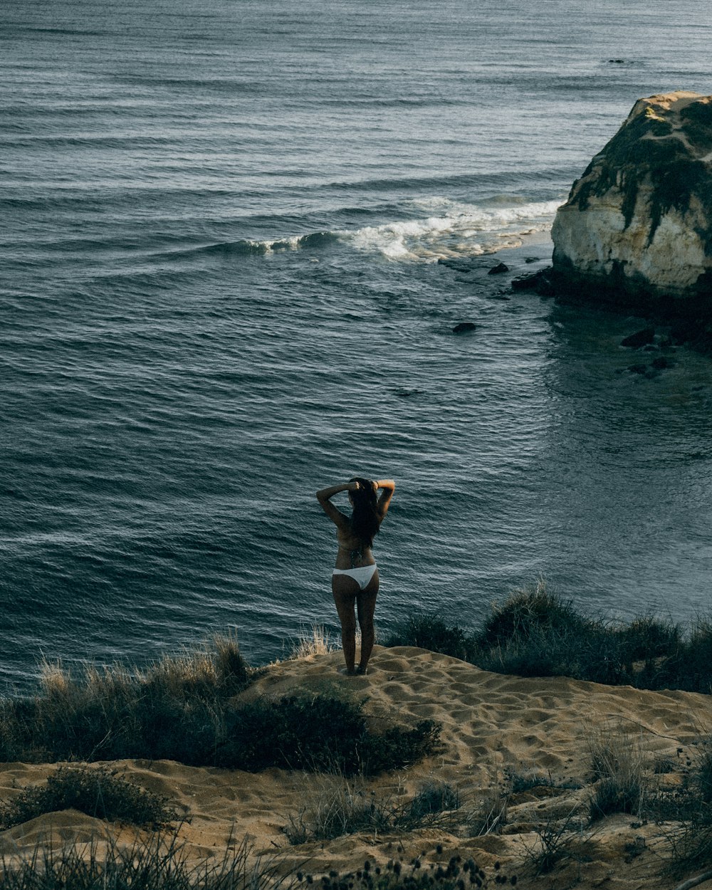 woman in black bikini standing on rock near sea during daytime