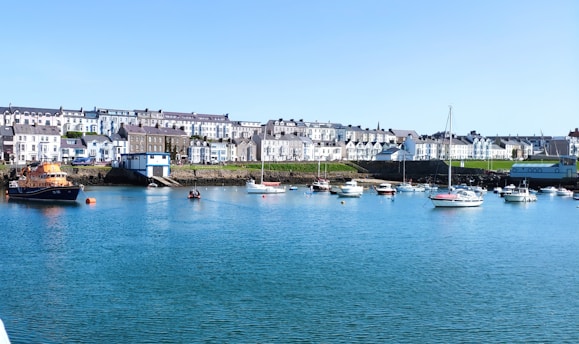 A cozy New England coastal home bathed in soft morning light with sailboats gently rocking in the harbor beyond.