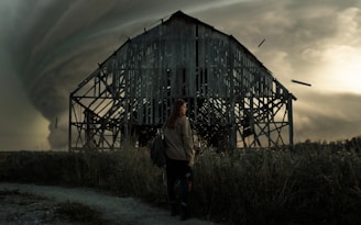 man in white long sleeve shirt standing beside brown wooden barn