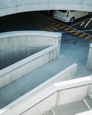 A concrete parking structure with ramps and barriers is visible, featuring a white vehicle parked against a backdrop of yellow-striped markings on the asphalt. The scene suggests an urban environment with an industrial design.