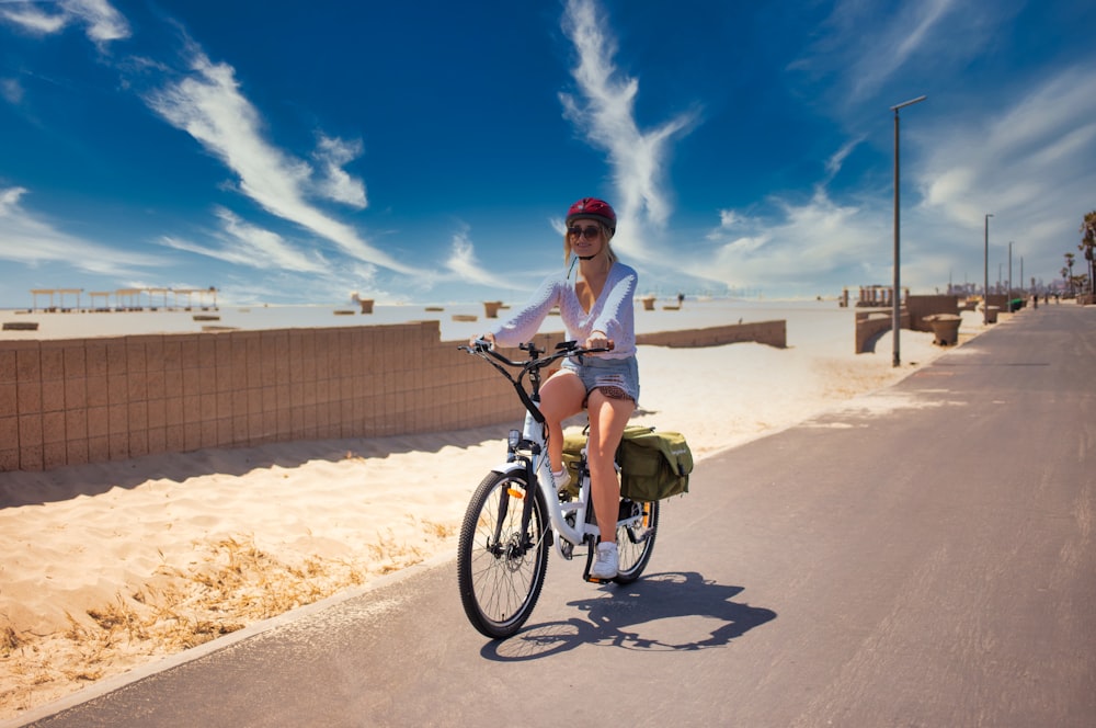 man in white polo shirt riding on black bicycle on brown sand during daytime