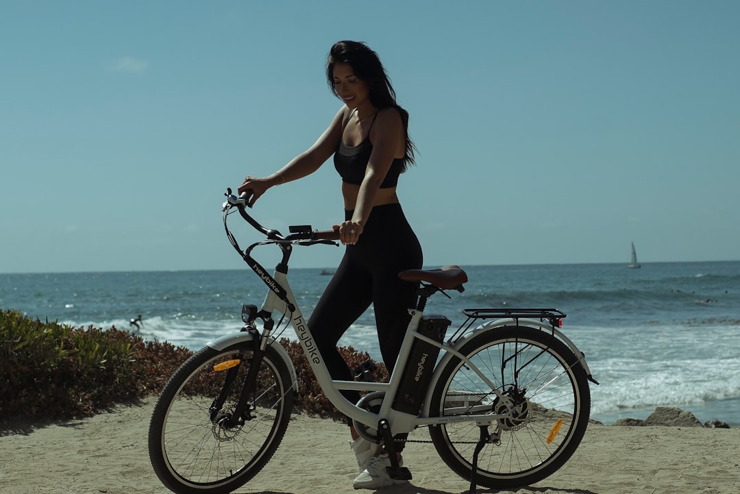 woman in brown tank top and blue denim shorts riding black bicycle near sea during daytime