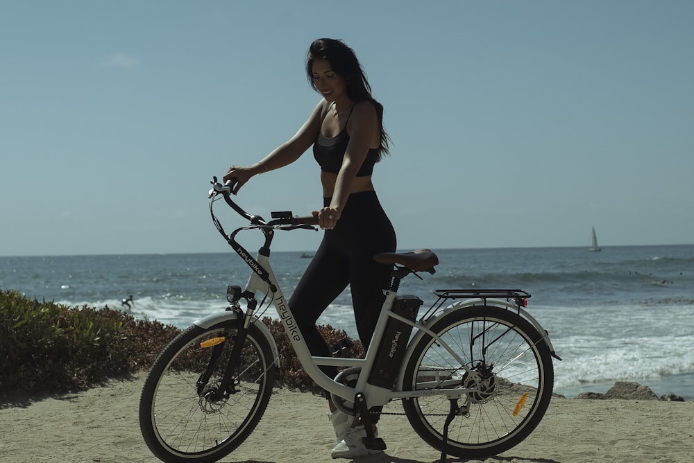 woman in brown tank top and blue denim shorts riding black bicycle near sea during daytime