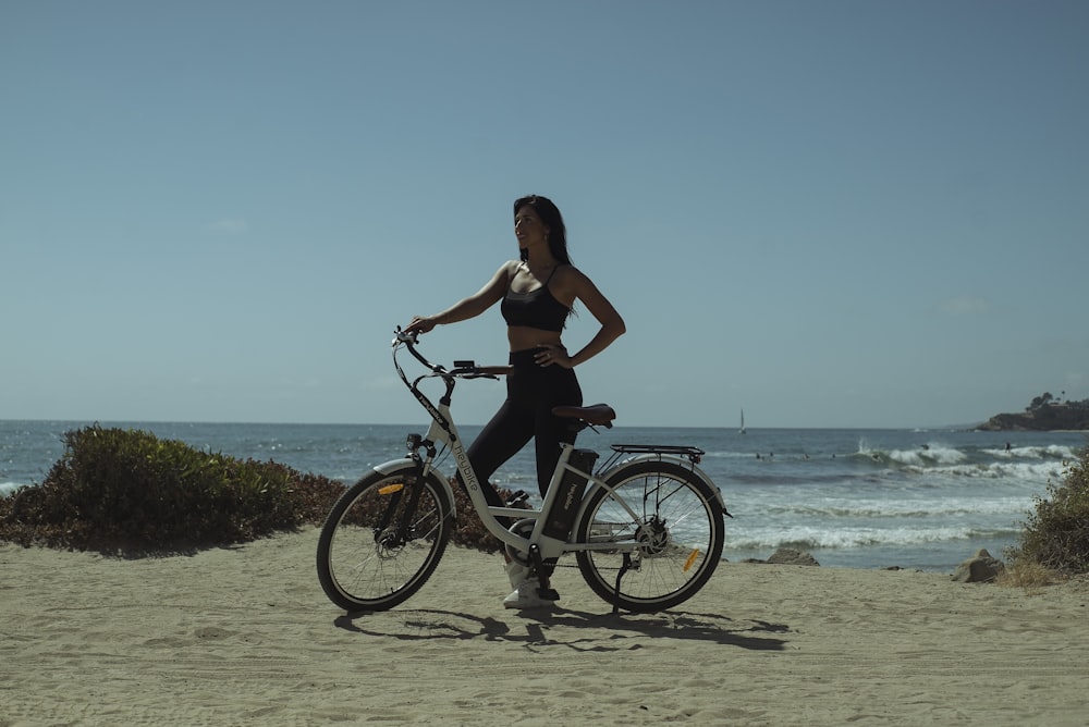 woman in black tank top riding on black bicycle on beach during daytime