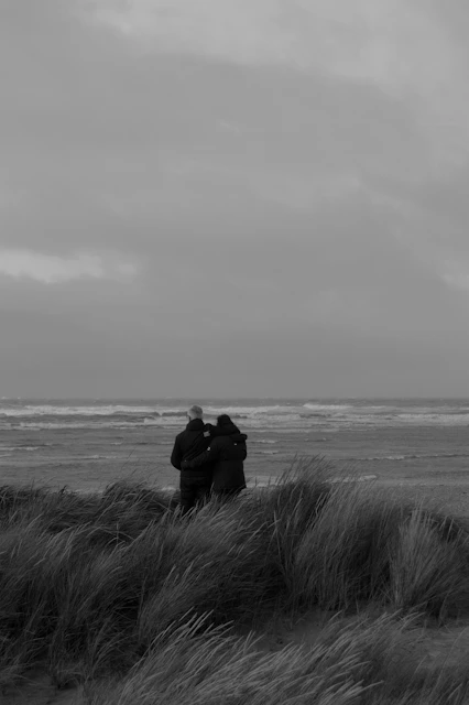 grayscale photo of couple sitting on grass near sea