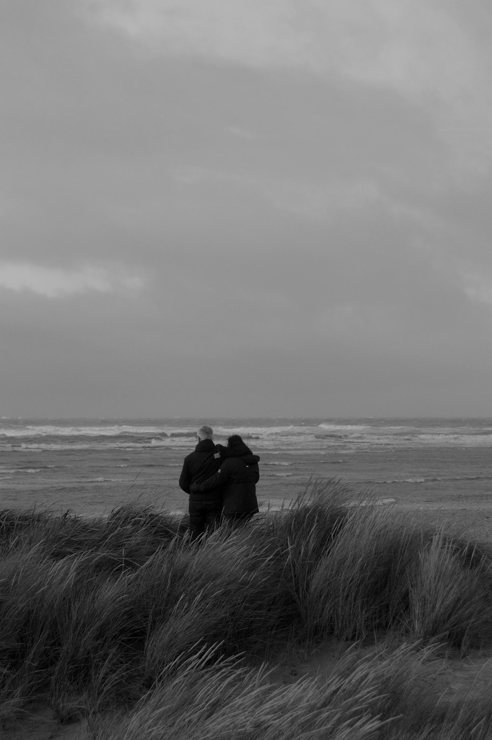grayscale photo of couple sitting on grass near sea