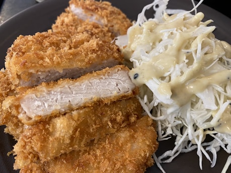 A close-up view of crispy, golden-brown breaded chicken slices arranged next to a serving of shredded cabbage drizzled with creamy dressing.