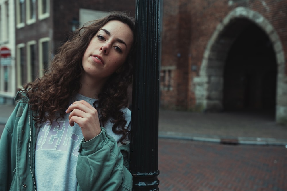 woman in green long sleeve shirt standing beside black metal post during daytime