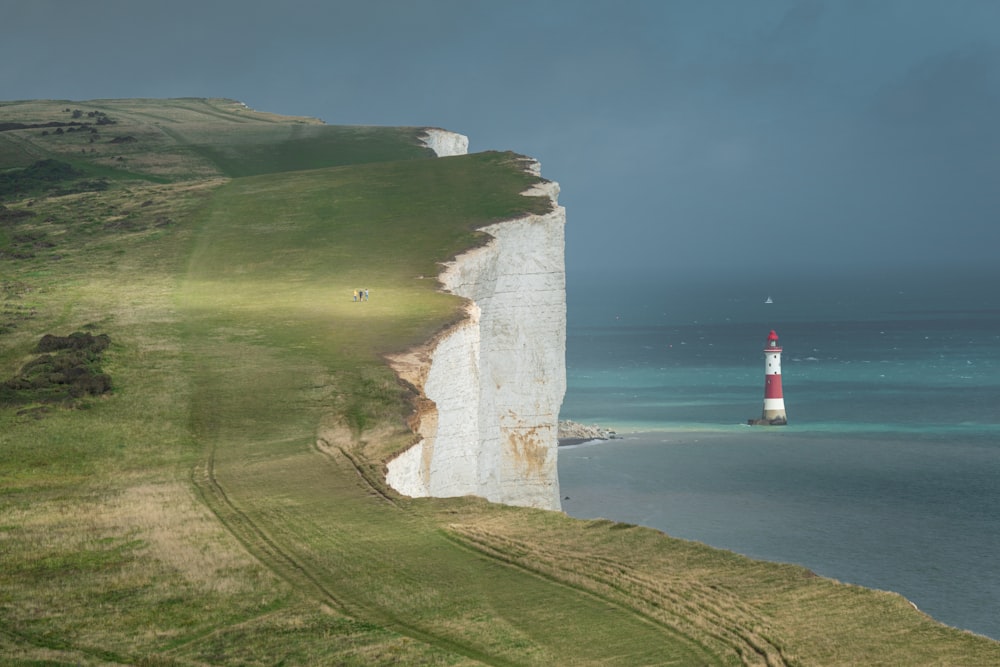 red and white lighthouse on green grass field near body of water during daytime