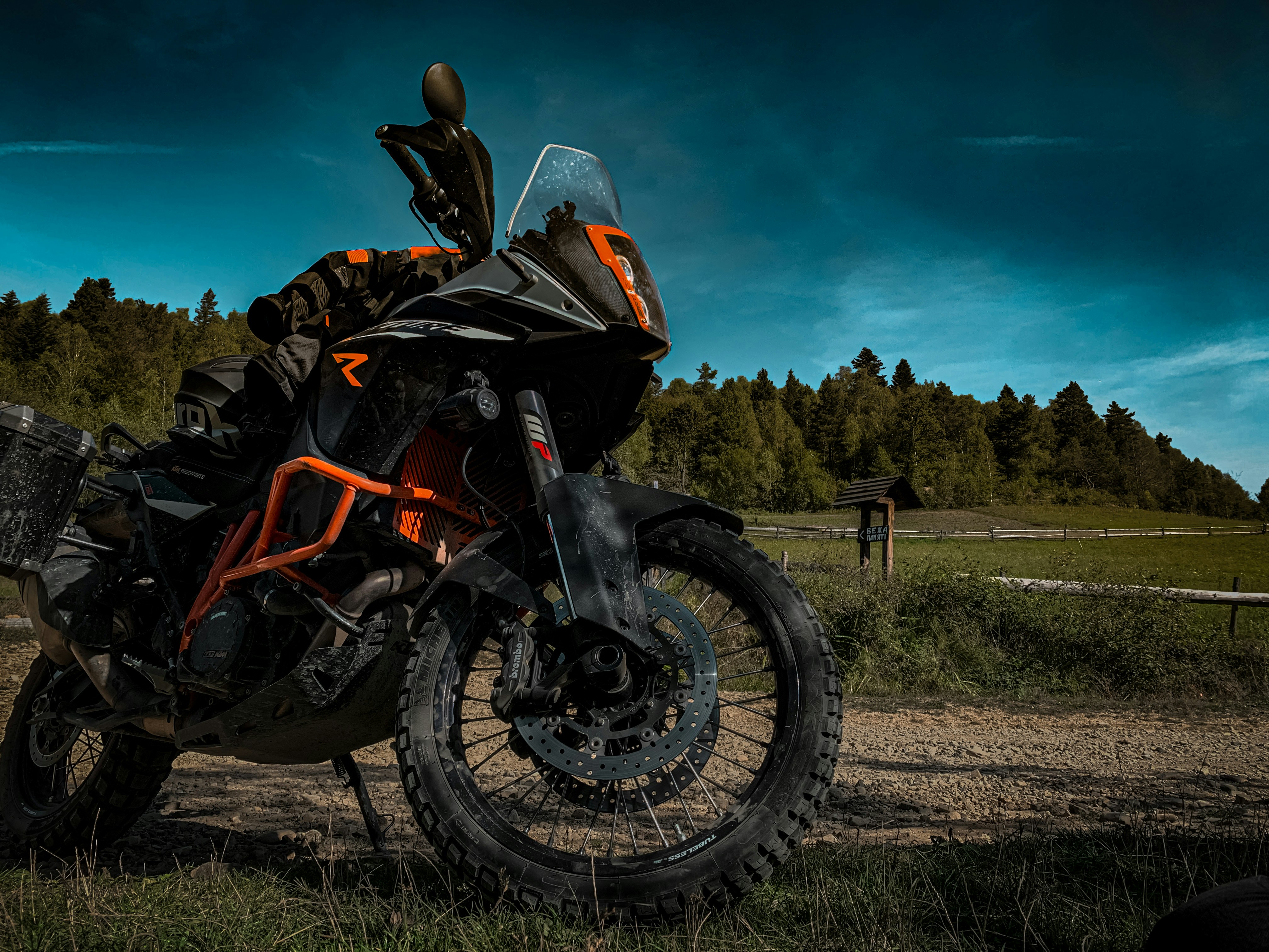 Orange adventure motorcycle with panniers, tall windscreen, knobby tires, rugged mountain backdrop, ready for off-road