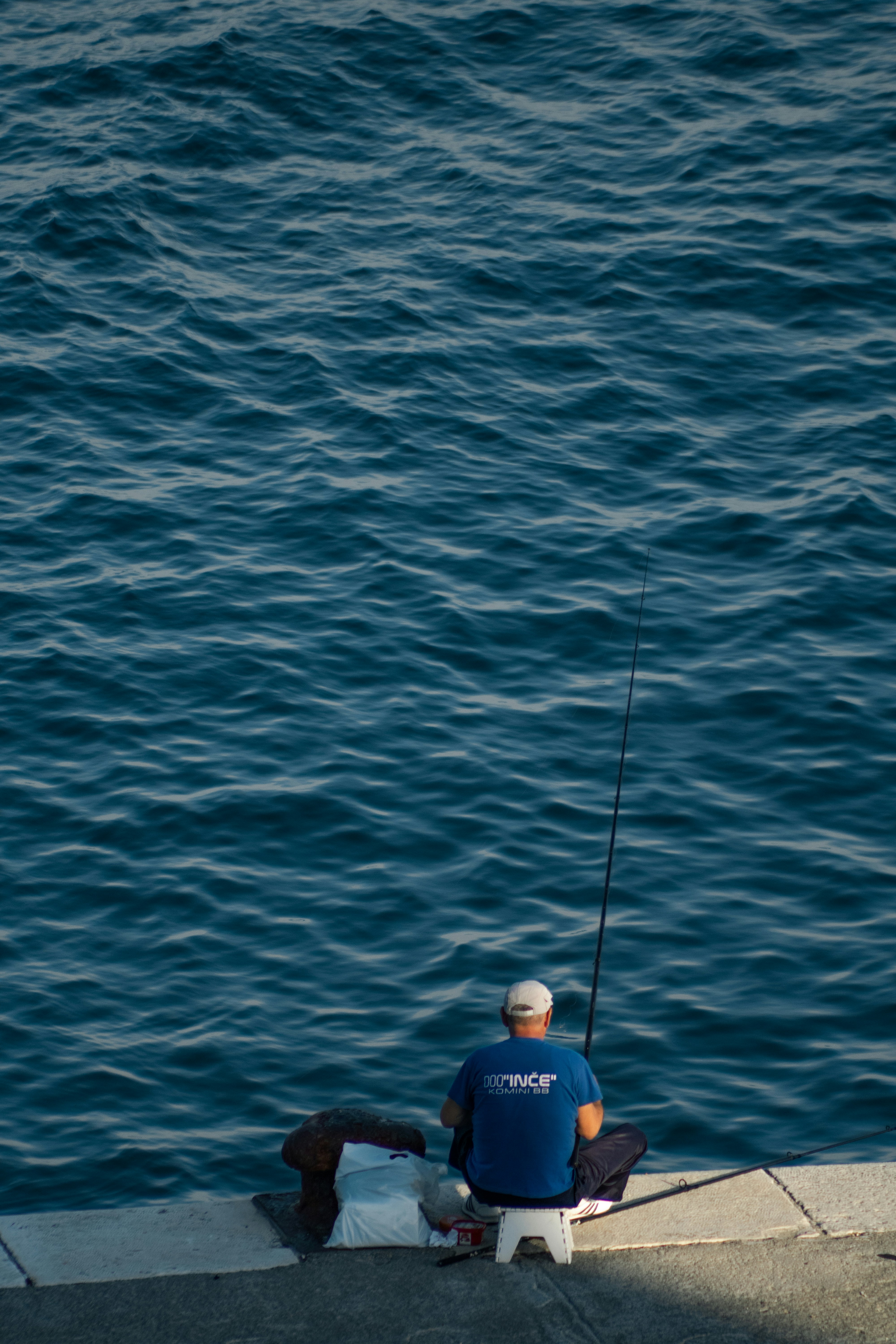 man in blue shirt fishing on blue sea during daytime