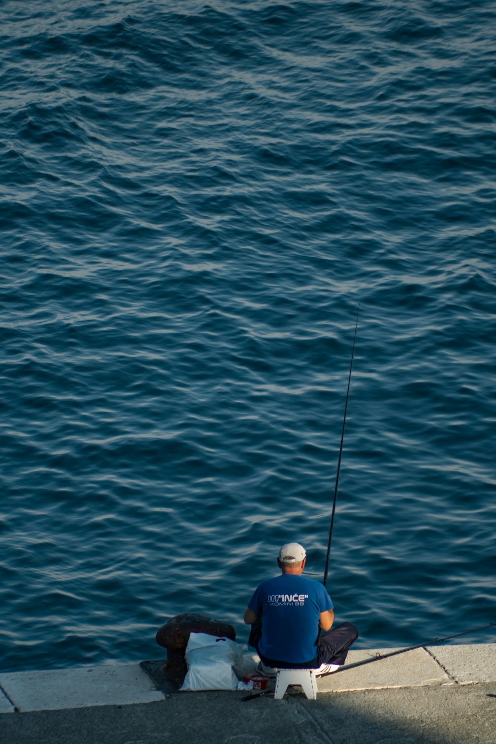 昼間、青い海で釣りをする青いシャツを着た男