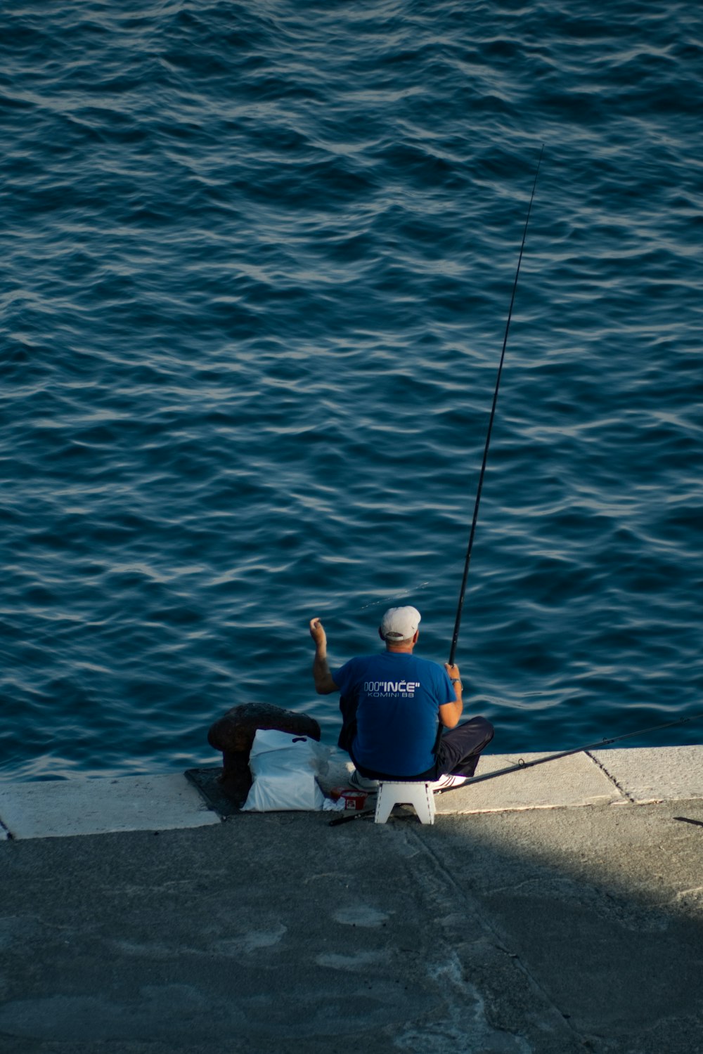 man in blue t-shirt and white shorts sitting on concrete dock during daytime