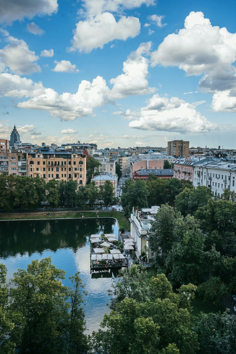 brown concrete building near green trees and river under white clouds and blue sky during daytime