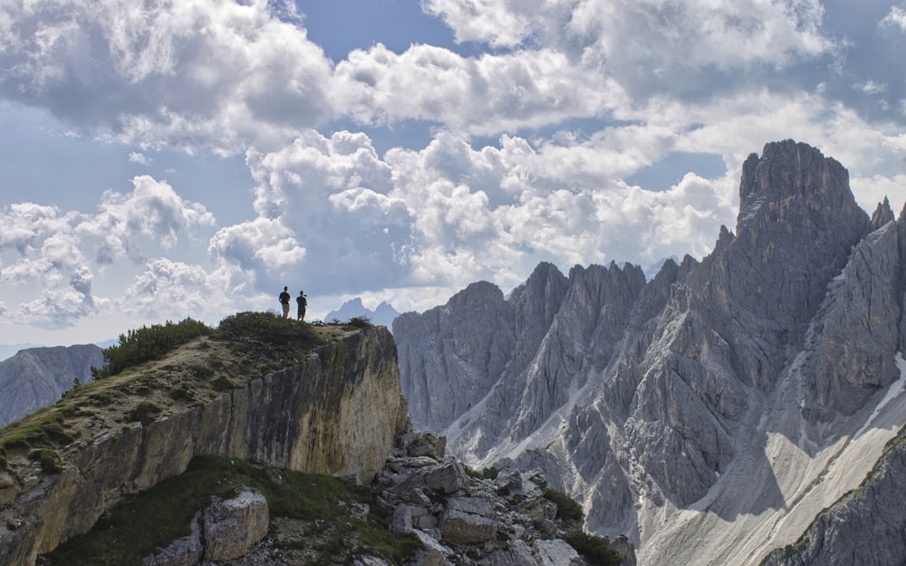 person standing on rocky mountain under white clouds during daytime