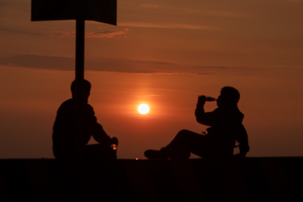 Silhouette von Menschen, die bei Sonnenuntergang auf der Bank sitzen
