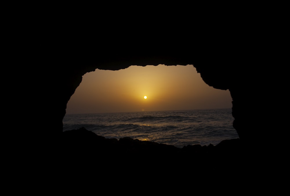 silhouette of cave near body of water during sunset