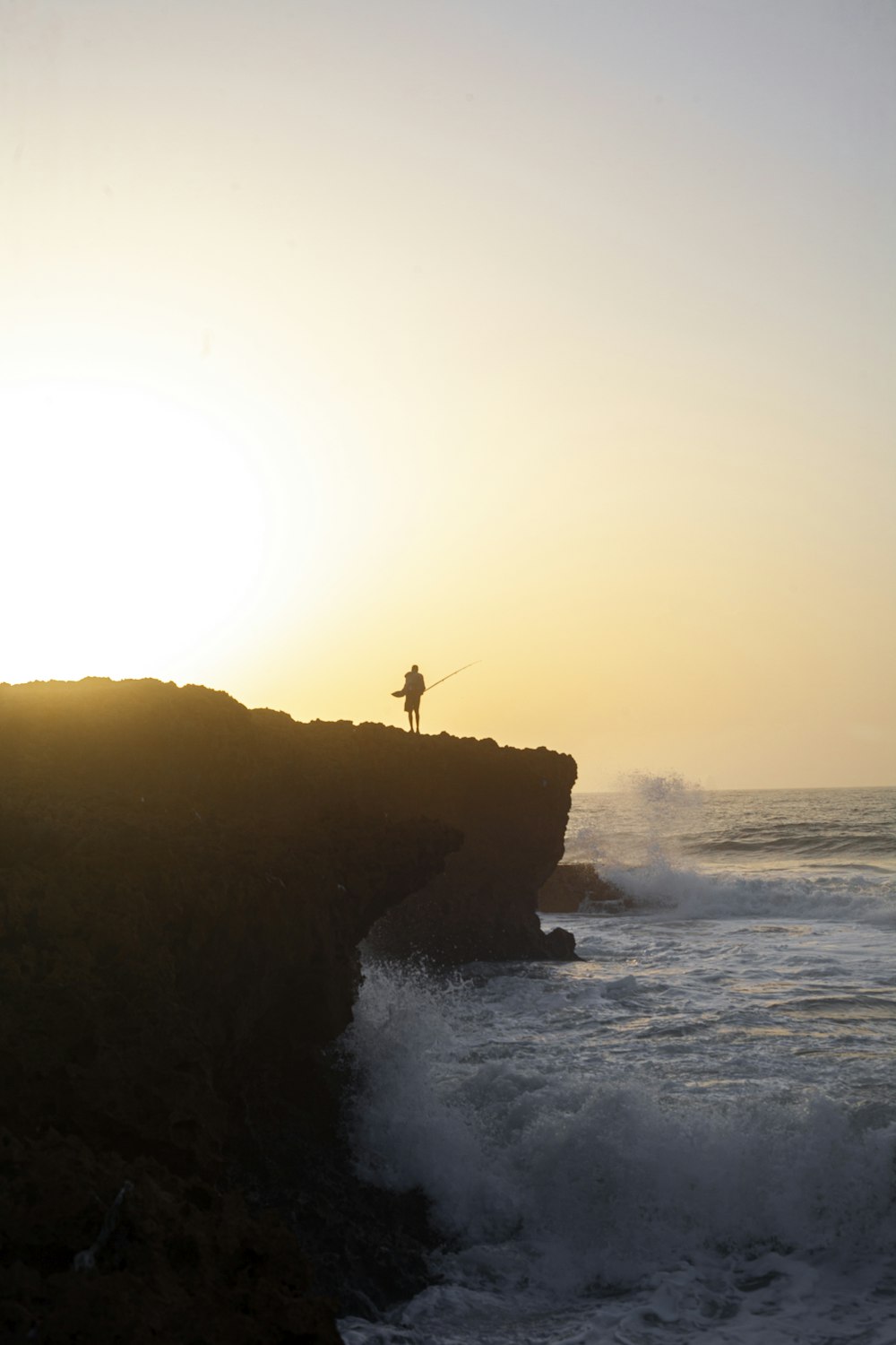 silhouette of person standing on rock formation near body of water during daytime