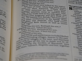 A close-up view of a page from a book with text describing genealogy. The text includes names and familial relationships written in a traditional serif font. The layout is typical of a religious or historical text with numbers denoting verses or sections.