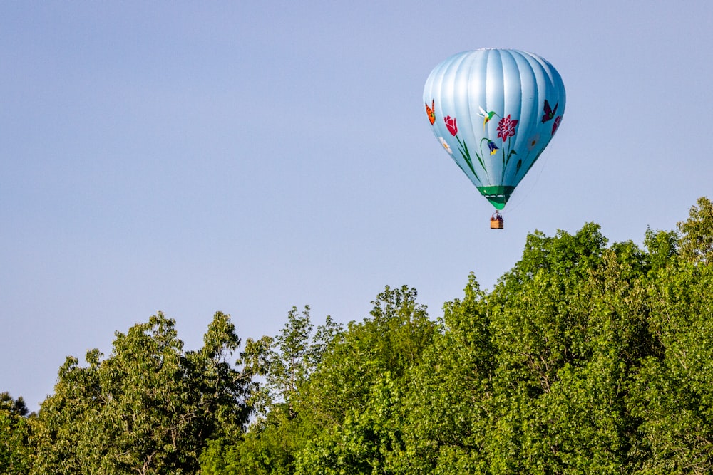 green and red hot air balloon flying over green trees during daytime