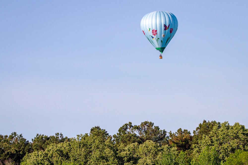 green blue and red hot air balloon flying over green trees during daytime