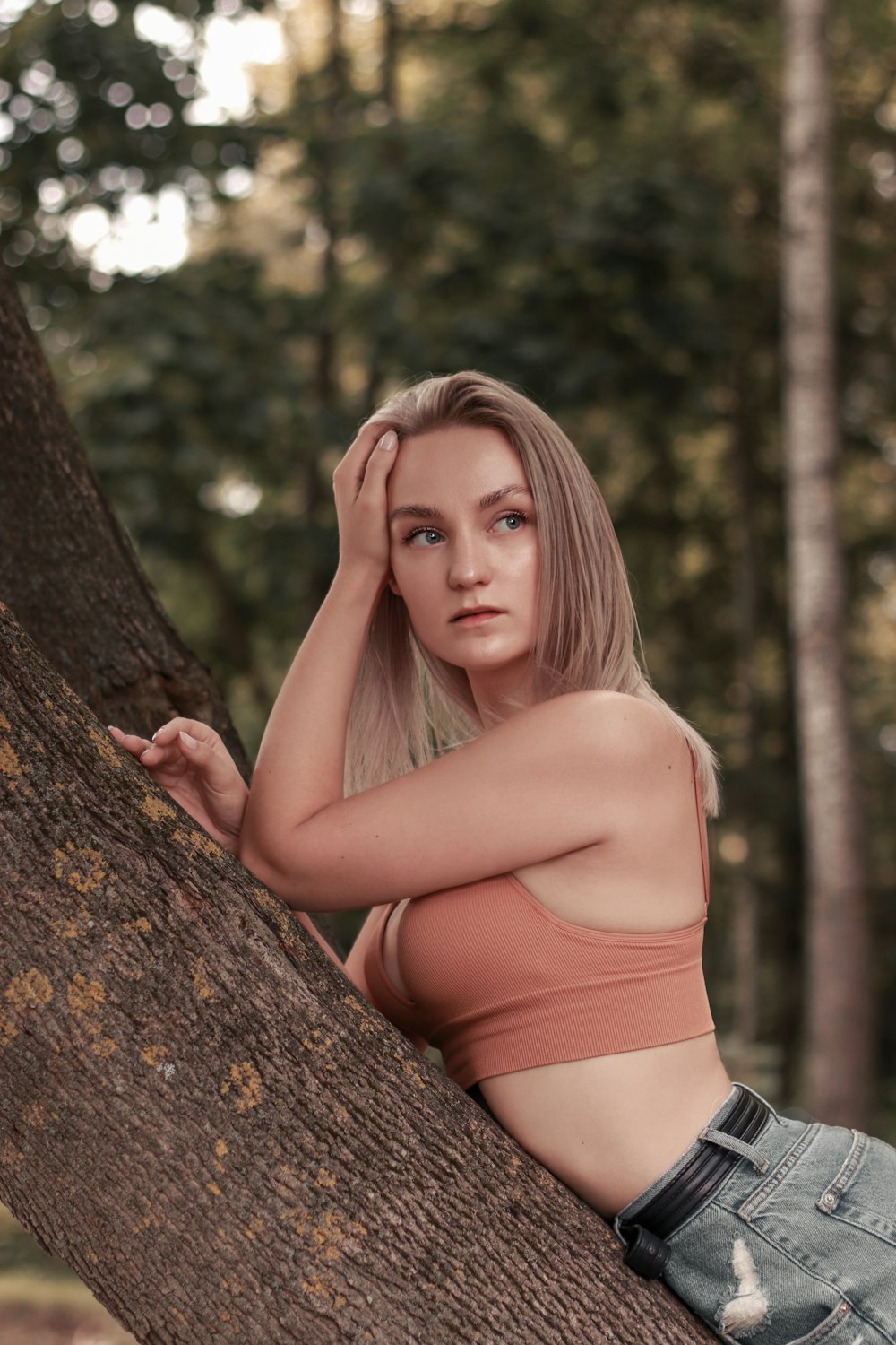 woman in orange tank top leaning on brown tree trunk