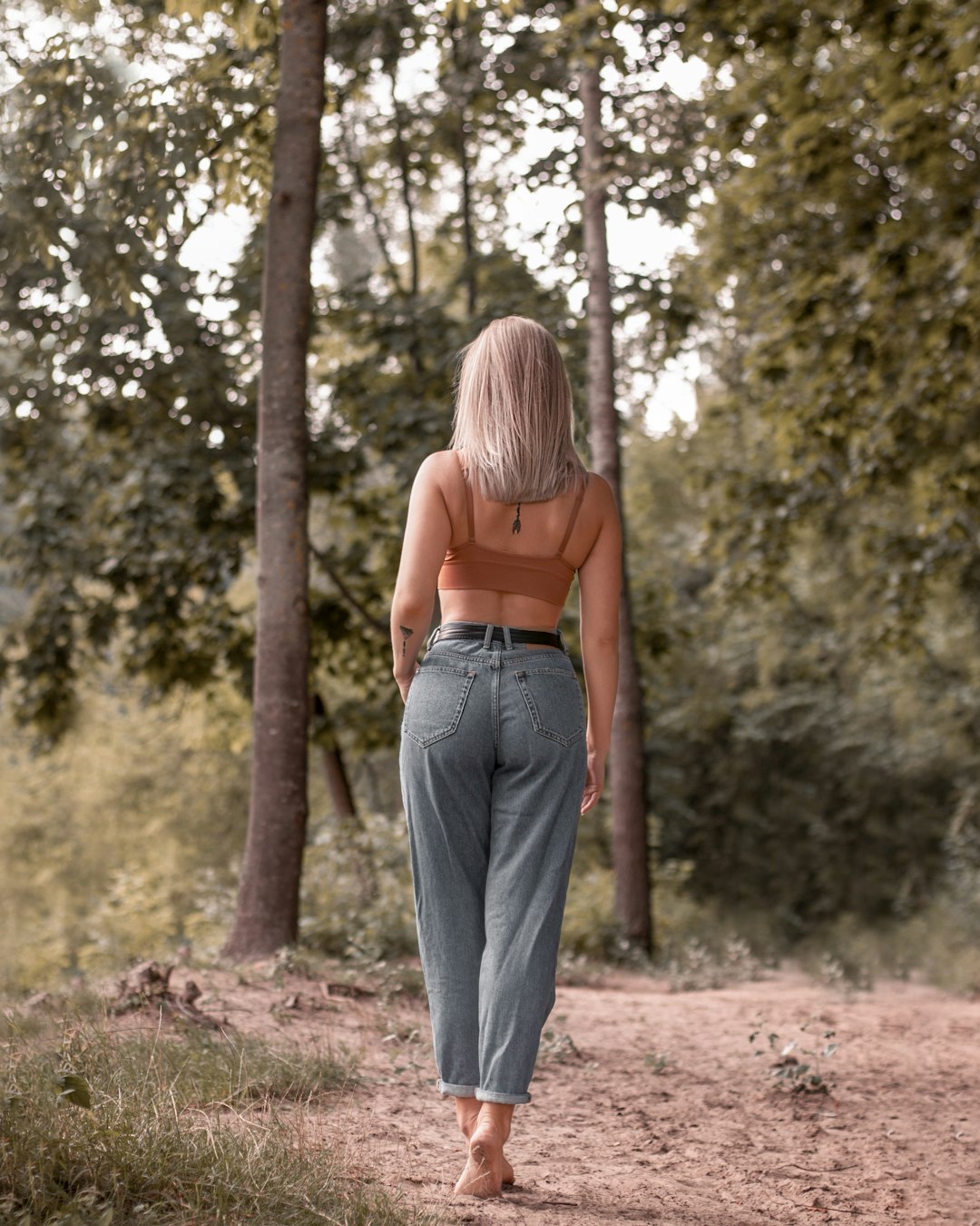 woman in brown tank top and blue denim jeans standing on brown dirt road during daytime