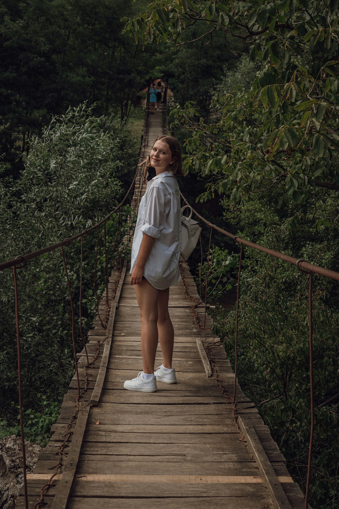 woman in white shirt walking on hanging bridge