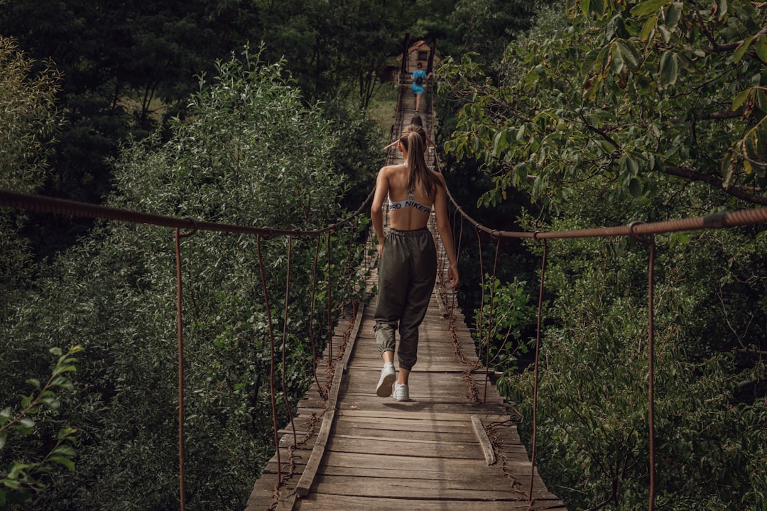 woman in brown jacket and blue denim jeans walking on hanging bridge