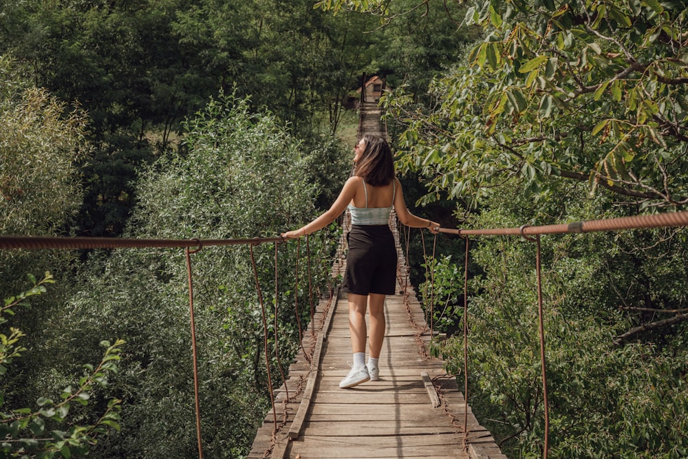 Frau in schwarzem Tanktop und weißen Shorts geht tagsüber auf einer Hängebrücke