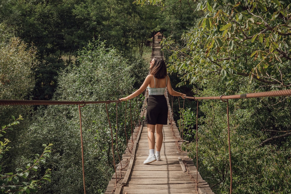 woman in black tank top and white shorts walking on hanging bridge during daytime
