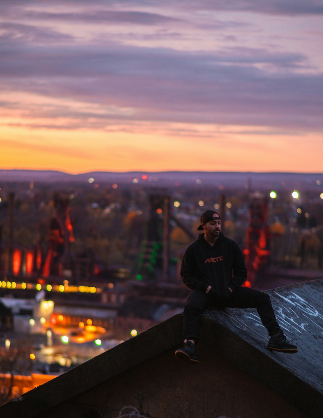 man in black hoodie sitting on black concrete fence during night time