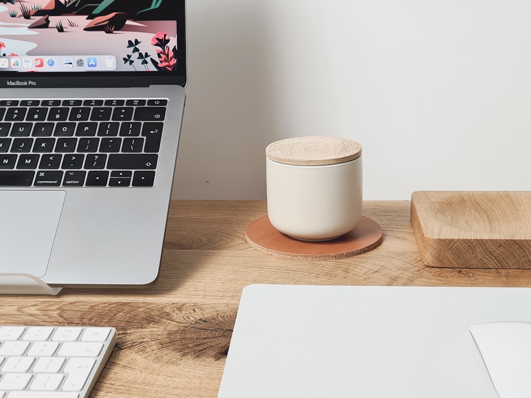 macbook pro beside white ceramic mug on brown wooden table