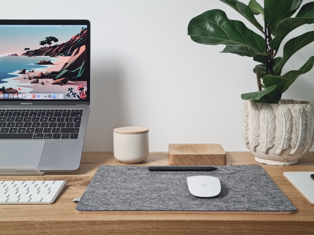 macbook pro ao lado da tábua de cortar de madeira marrom e caneca de cerâmica branca na mesa de madeira marrom