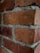 Red bricks arranged in a wall pattern with visible mortar in between, showing a textured surface and weathered appearance.