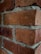 Red bricks arranged in a wall pattern with visible mortar in between, showing a textured surface and weathered appearance.