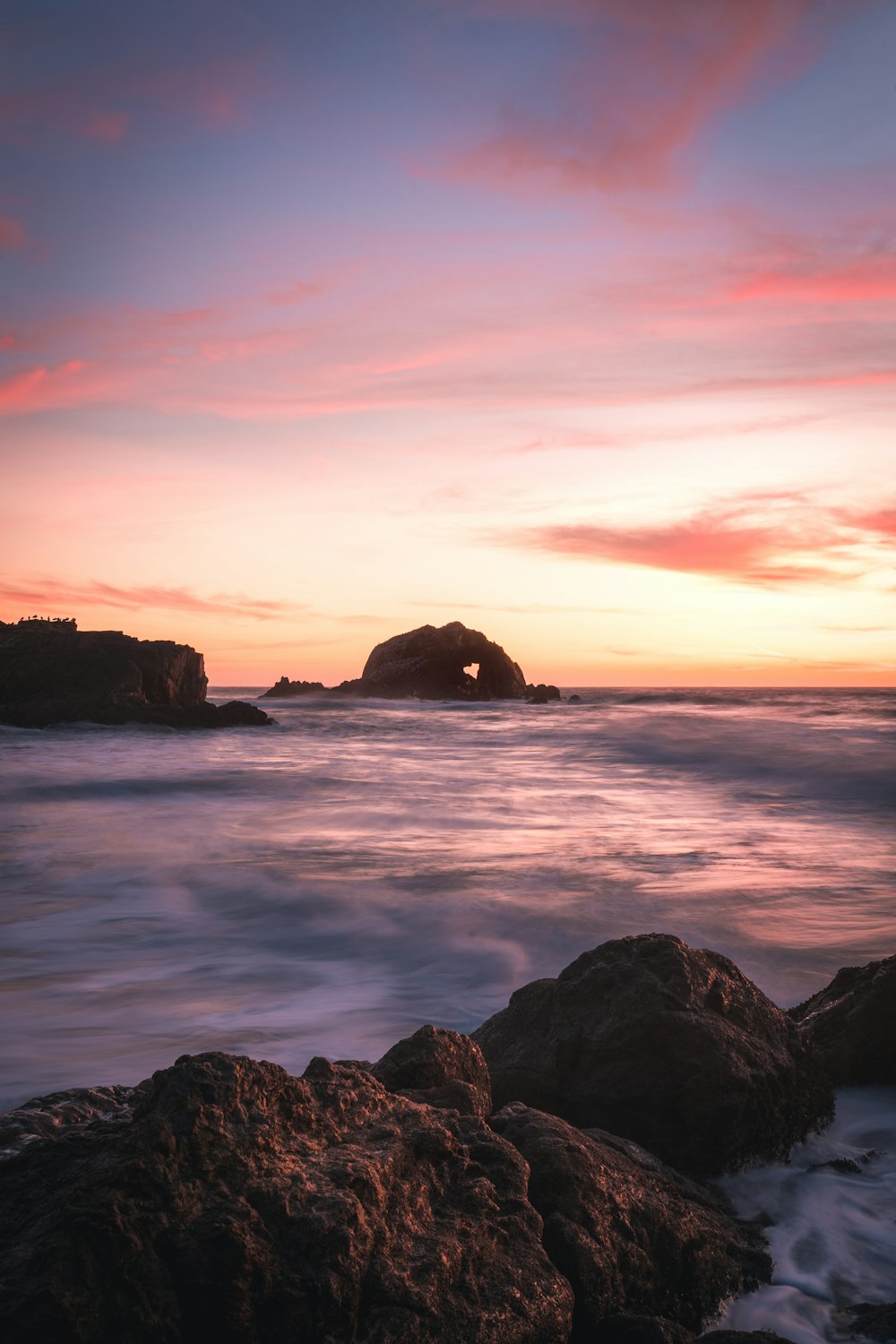 silhouette of rock formation on sea during sunset