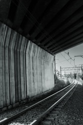 A mentor and young engineer discussing project drawings beside a railway bridge.