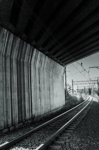A mentor and young engineer discussing project drawings beside a railway bridge.