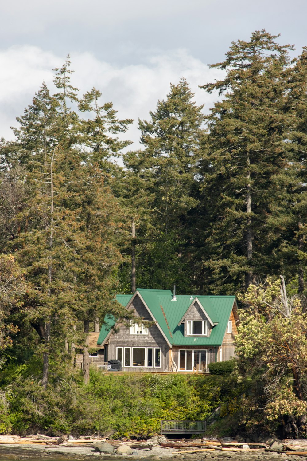 grünes und weißes Holzhaus, umgeben von grünen Bäumen unter weißen Wolken und blauem Himmel während