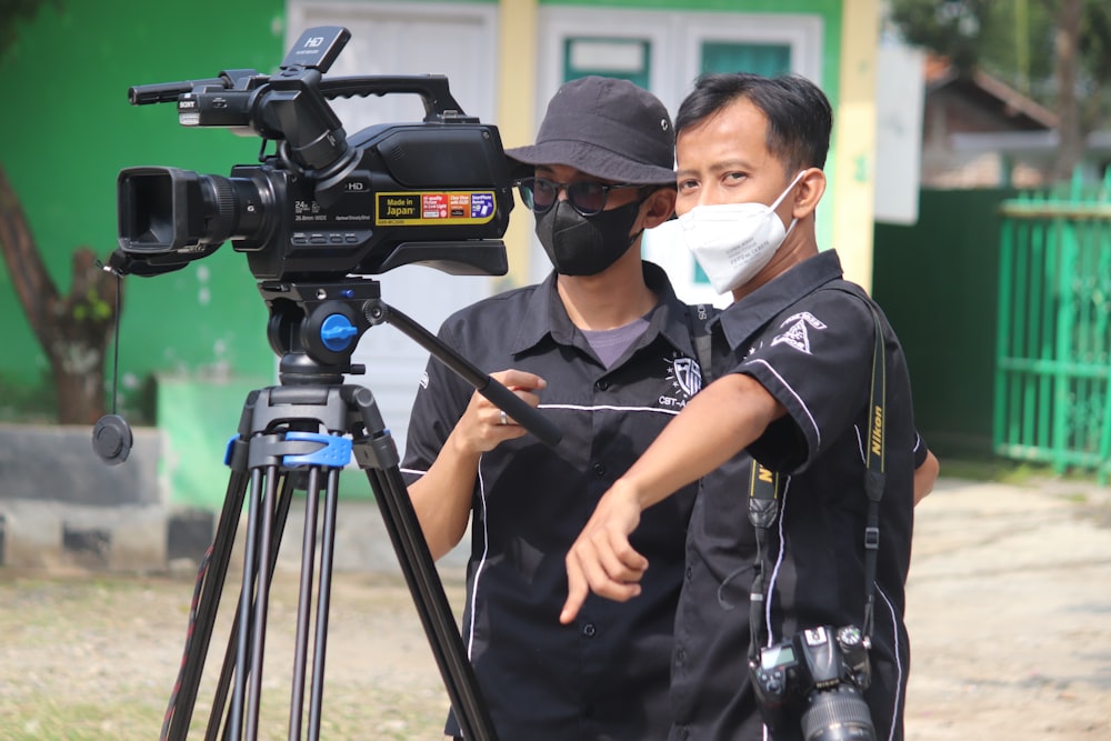 man in black polo shirt wearing white mask holding black camera